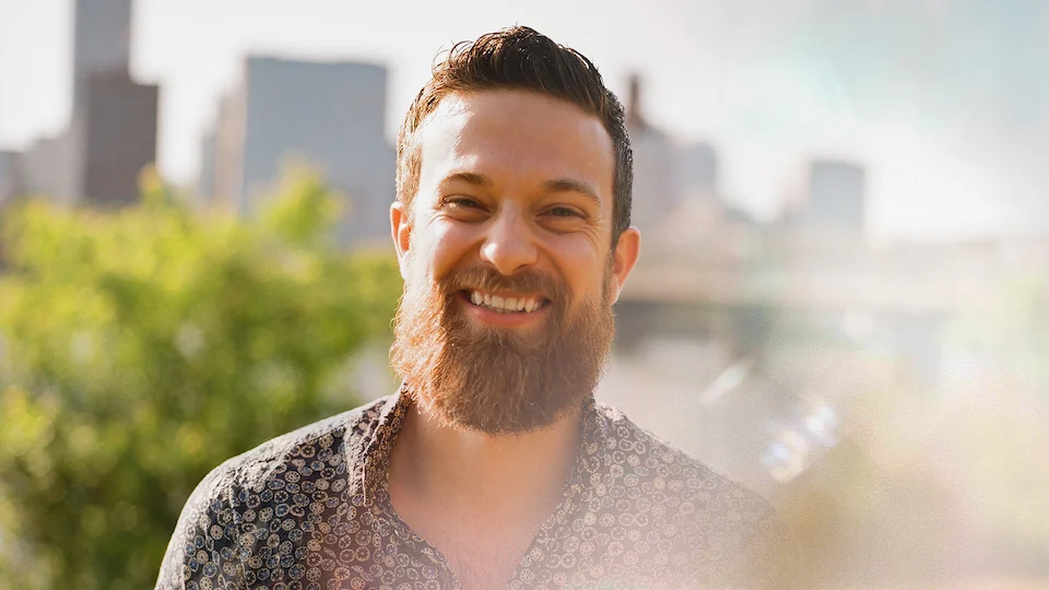 Keith Gilmore smiling in front of a city skyline in the sun
